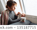 young woman warms up with hot tea in winter weather at home 135187715