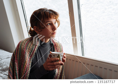 young woman warms up with hot tea in winter weather at home 135187717