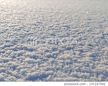 Blurred sparkling snow surface abstract. Soft defocused white snow texture with sunlight bokeh and sparkles, dreamy winter background overlay. 135187992