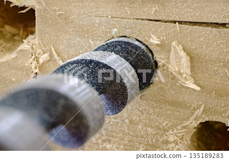 A drill makes a hole in a wooden board A drill makes a hole in a wooden board 135189283