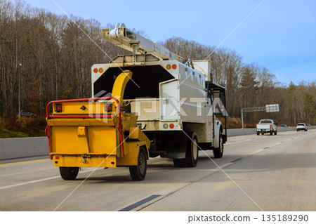 Utility truck pulls yellow trailer on highway with few vehicles, in American rural setting Utility truck pulls yellow trailer on highway with few vehicles, in American rural setting 135189290