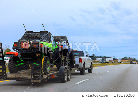 Truck pulls trailer with two off road vehicles down busy American highway with other vehicles are nearby. 135189296