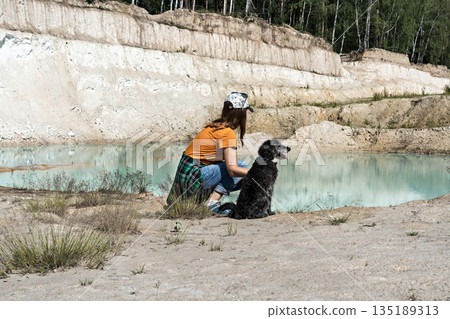 Young woman traveler in cap in ginger walking on sandy shore of blue lake or river with fluffy gray dog, active lifestyle, travel with pets Young woman traveler in cap in ginger walking on sandy shore of blue lake or river with fluffy gray dog, active lifestyle, travel with pets 135189313