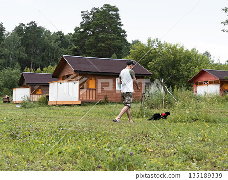 young man in cap walking with black cat in red harness on leash on green grass, friendship pet love and care young man in cap walking with black cat in red harness on leash on green grass, friendship pet love and care 135189339