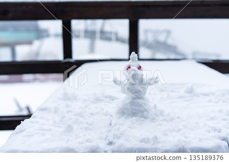 Tiny snow figure placed on snow-covered table. Winter fun concept with snowman Tiny snow figure placed on snow-covered table. Winter fun concept with snowman 135189376