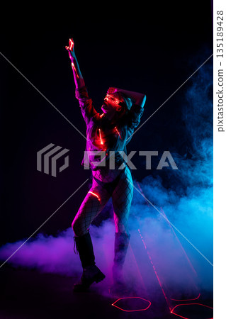 Futuristic woman in LED glasses dancing in neon lights with laser beams and smoke Futuristic woman in LED glasses dancing in neon lights with laser beams and smoke 135189428