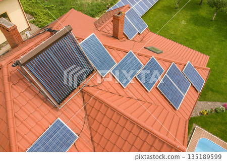 Aerial view of a new autonomous house with solar panels and water heating radiators on the roof. Aerial view of a new autonomous house with solar panels and water heating radiators on the roof. 135189599