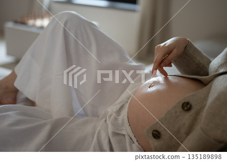 Pregnant woman relaxing on bed touching her belly 135189898