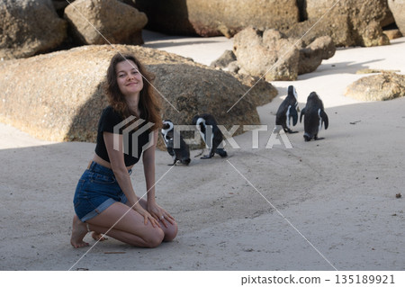 Tourist kneeling on Boulders Beach interacting with african penguins Tourist kneeling on Boulders Beach interacting with african penguins 135189921