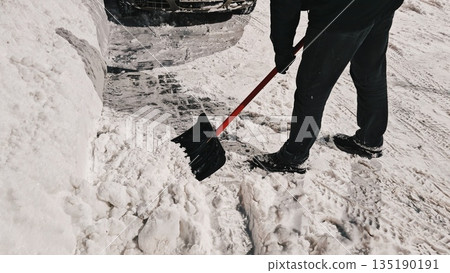 Clearing snow with a shovel in the winter on the street. a view of a person shoveling snow in the evening during winter Clearing snow with a shovel in the winter on the street. a view of a person shoveling snow in the evening during winter 135190191