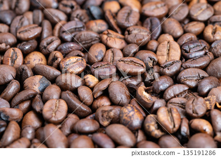 Detailed medium roast beans displaying glossy finish and warm hues, Macro image of varying roasted coffee beans showcasing rich brown shades and matte surface texture 135191286