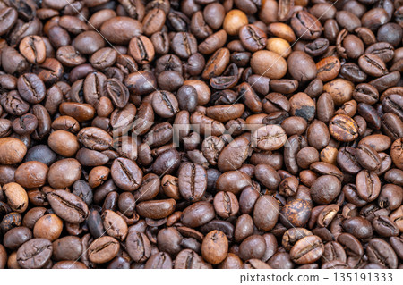 Closeup of roasted coffee beans, Detailed view of glossy roasted coffee beans on tray surface, Close examination of polished roasted coffee beans illuminated softly on tray 135191333