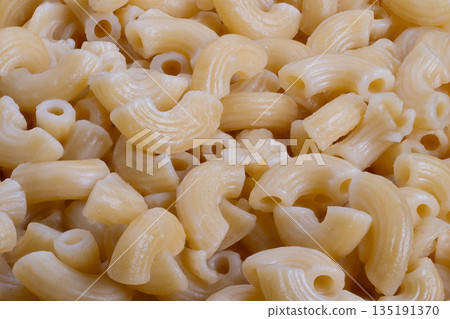 Closeup golden macaroni curves evoke childhood comfort and school lunch memories, warm lighting and tactile surface create cozy mood for editorial and lifestyle campaigns 135191370