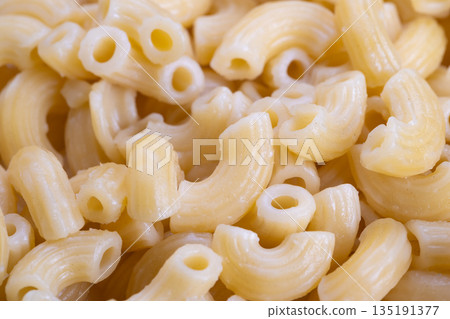 Beautiful pasta closeup, Shiny elbow macaroni detail, High contrast image of glossy pasta surfaces, Closeup photograph highlighting uniform smoothness of boiled elbow pasta Beautiful pasta closeup, Shiny elbow macaroni detail, High contrast image of glossy pasta surfaces, Closeup photograph highlighting uniform smoothness of boiled elbow pasta 135191377