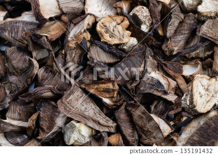 Detailed view of dried mushrooms stored in natural wooden bowl setting, Closeup shot of preserved dried mushrooms arranged in rustic wooden vessel for culinary use Detailed view of dried mushrooms stored in natural wooden bowl setting, Closeup shot of preserved dried mushrooms arranged in rustic wooden vessel for culinary use 135191432