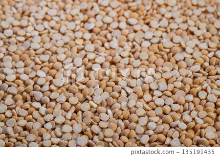 Yellow split peas close up revealing coarse groats texture, rustic pantry mood, warm beige tones, scattered pattern ideal for ingredient photography and recipe concept 135191435