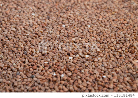 Close up buckwheat groats texture, earthy brown kernels scattered across flat surface, shallow depth of field, natural lighting, crisp detail for food packaging and social media Close up buckwheat groats texture, earthy brown kernels scattered across flat surface, shallow depth of field, natural lighting, crisp detail for food packaging and social media 135191494