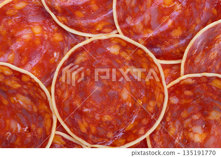 Closeup chorizo slices showing vibrant marbling and glossy surface, cured sausage rings overlapping to create bold red pattern ideal for food packaging and culinary backgrounds 135191770