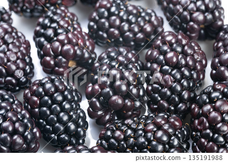 Close view of blackberry drupelet surface features, Highresolution photograph showcasing textured surface and reflective highlights of ripe blackberries in dense cluster 135191988