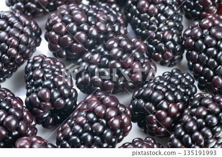 Highcontrast macro image of fresh glossy blackberries, Detailed macro photograph showcasing shiny blackberries on white background for marketing and culinary use Highcontrast macro image of fresh glossy blackberries, Detailed macro photograph showcasing shiny blackberries on white background for marketing and culinary use 135191993
