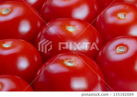 Glossy red cherry tomatoes closeup piled tightly, smooth skins and bright highlights, saturated color suggests freshness and abundance, perfect for market, packaging, advertising 135192084