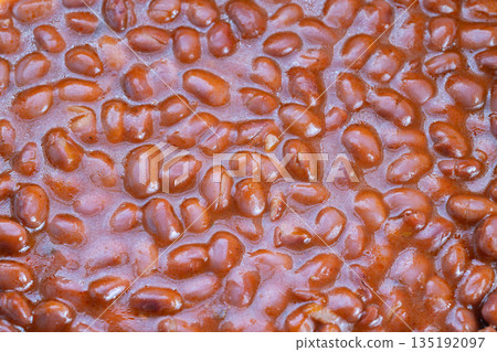 Closeup saucy red beans simmering in rich tomato glaze, glossy skins, warm homestyle kitchen vibe, wooden spoon implied, steam, hearty comfort food, family dinner 135192097
