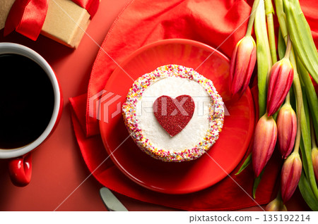 Valentine's Day festive red background. Cake with red heart, cup of coffee, gift box and spring red tulip flower bouquet. Top view Valentine's Day festive red background. Cake with red heart, cup of coffee, gift box and spring red tulip flower bouquet. Top view 135192214