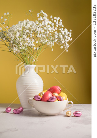 Easter chocolate colourful eggs in a bowl and gypsophila flowers in a vase. Spring holiday background. Easter chocolate colourful eggs in a bowl and gypsophila flowers in a vase. Spring holiday background. 135192238