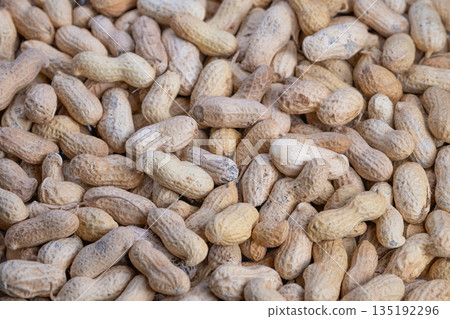 Closeup of shelled peanuts recreation, Rustic market scene featuring heap of raw peanuts, Close view showcases rough peanut shells amidst bustling farm market environment 135192296