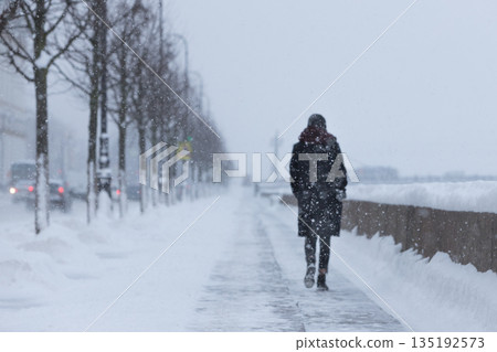 Silhouette of woman walking on street during snowfall. Heavy blizzard in European city Silhouette of woman walking on street during snowfall. Heavy blizzard in European city 135192573