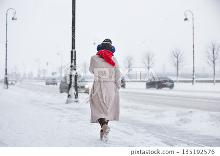 Woman walking on street during snowfall. Heavy snowfall and winter time European city Woman walking on street during snowfall. Heavy snowfall and winter time European city 135192576