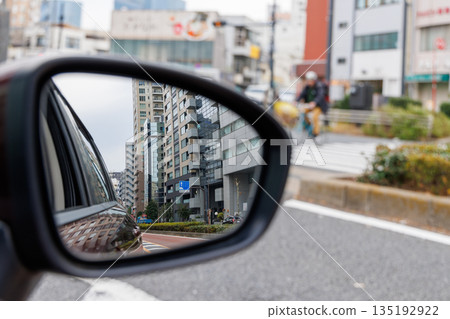 A side mirror of a moving car reflecting urban traffic congestion and cityscape 135192922
