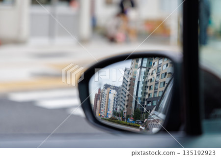A side mirror of a moving car reflecting urban traffic congestion and cityscape A side mirror of a moving car reflecting urban traffic congestion and cityscape 135192923