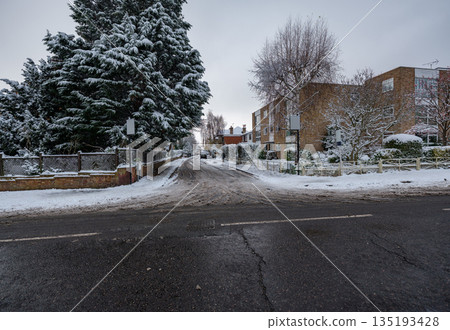 Quiet residential neighbourhood in winter with snow-covered road, parked cars and sidewalks illustrating seasonal cold weather conditions. 135193428