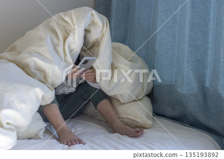 Image of a girl in a dimly lit room, covered with a blanket, looking at a smartphone (5 years old, Japanese, no face) Image of a girl in a dimly lit room, covered with a blanket, looking at a smartphone (5 years old, Japanese, no face) 135193892