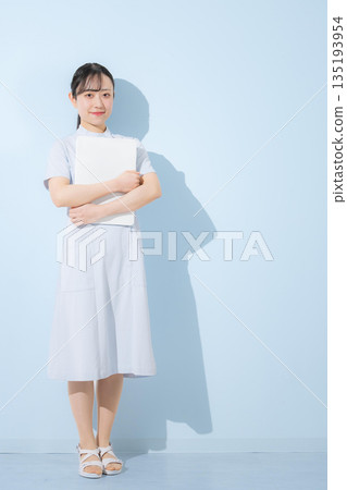 Nurse holding a laptop or tablet on a light blue background, looking at the camera. Image for job change or recruitment. Full body. Nurse holding a laptop or tablet on a light blue background, looking at the camera. Image for job change or recruitment. Full body. 135193954