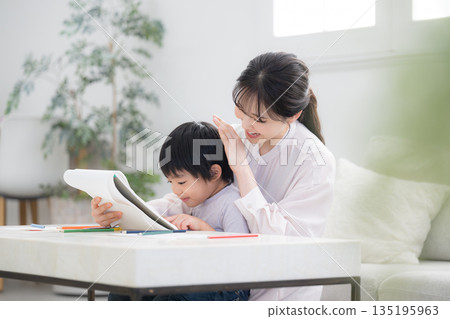 A toddler enjoys learning while being watched by his mother (mother) and opens his notebook. Praise the child. A toddler enjoys learning while being watched by his mother (mother) and opens his notebook. Praise the child. 135195963