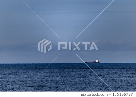 Distant Cargo Ship Against Expansive Ocean and Tranquil Sky 135196757