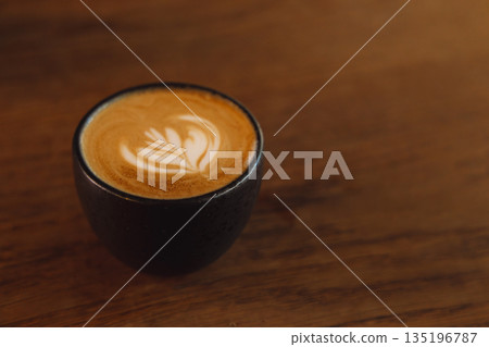 Latte Art Cappuccino in Black Cup on Warm Wooden Table Surface Latte Art Cappuccino in Black Cup on Warm Wooden Table Surface 135196787