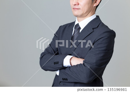 A middle-aged male businessman in a suit with his arms folded A middle-aged male businessman in a suit with his arms folded 135196981