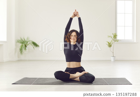 Young yogi sporty woman practicing yoga, stretching warm up doing exercise in easy seat pose Young yogi sporty woman practicing yoga, stretching warm up doing exercise in easy seat pose 135197288