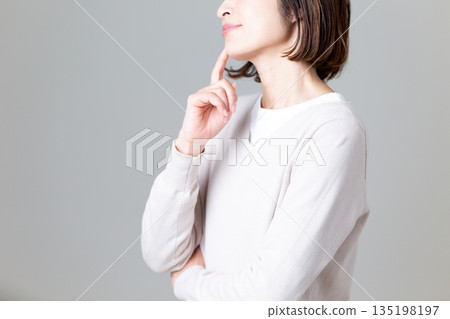 A middle-aged woman in casual knitwear thinking 135198197