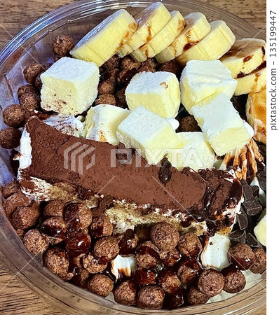 Swirled yogurt ice cream dessert served in a cup, smooth creamy texture with glossy surface, topped with fresh fruit pieces, highlighting its refreshing and inviting appearance in detail 135199447