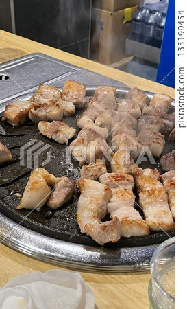 Grilled samgyeopsal, showcasing thick slices of pork belly sizzling on the grill. A popular Korean barbecue dish, capturing the essence of a delicious dining experience. Grilled samgyeopsal, showcasing thick slices of pork belly sizzling on the grill. A popular Korean barbecue dish, capturing the essence of a delicious dining experience. 135199454