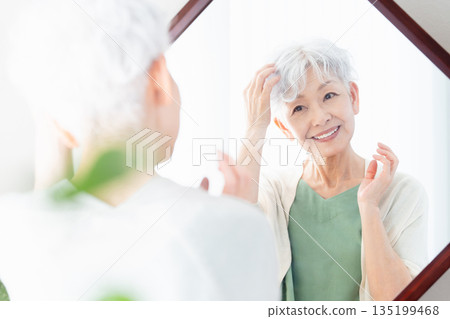 Senior woman styling her hair in front of the mirror Senior woman styling her hair in front of the mirror 135199468