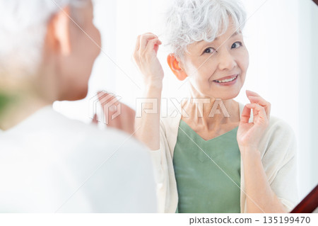 Senior woman styling her hair in front of the mirror Senior woman styling her hair in front of the mirror 135199470