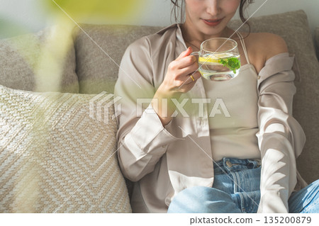 一位女士坐在沙發上喝檸檬水，排毒水 135200879