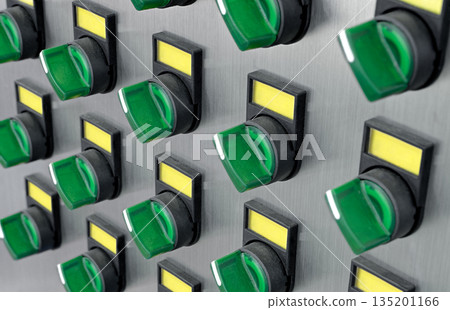 A lot of green electric switches with yellow labels on a brushed metal control panel 135201166