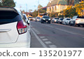 Rear side of white hatchback car parked on the roadside. Blurred cars driving on the road background in evening time with sunset light. Transportation concept. 135201977