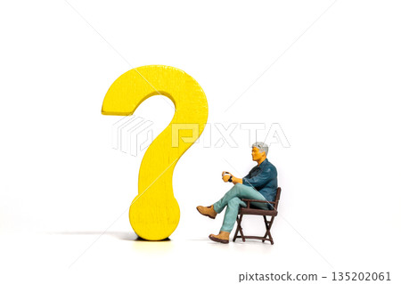 Miniature Man Sitting Beside Yellow Question Mark Miniature Man Sitting Beside Yellow Question Mark 135202061